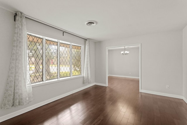 spare room featuring baseboards, a notable chandelier, visible vents, and dark wood-style flooring