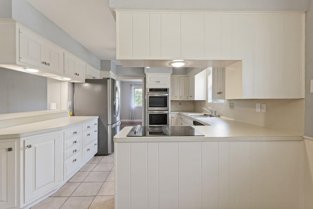 kitchen featuring light tile patterned floors, appliances with stainless steel finishes, a peninsula, light countertops, and a sink