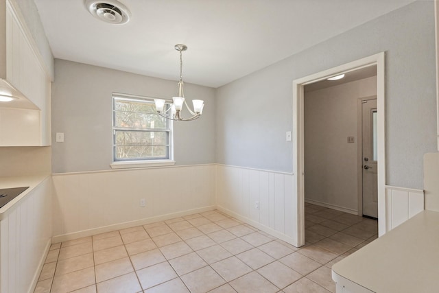 unfurnished dining area with light tile patterned floors, wainscoting, visible vents, and an inviting chandelier