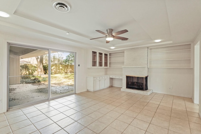 unfurnished living room with a tray ceiling, visible vents, a fireplace, and light tile patterned flooring