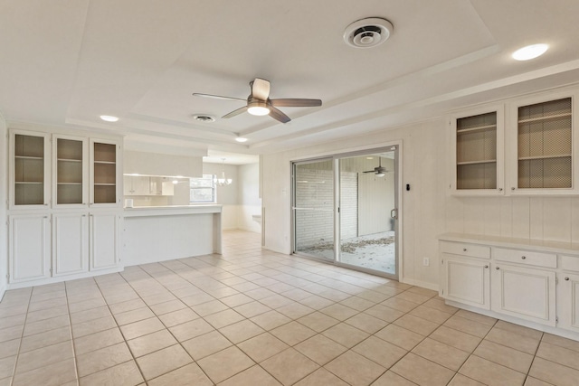 interior space featuring light tile patterned floors, visible vents, a raised ceiling, and ceiling fan with notable chandelier