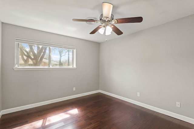 spare room with dark wood-type flooring, a ceiling fan, and baseboards