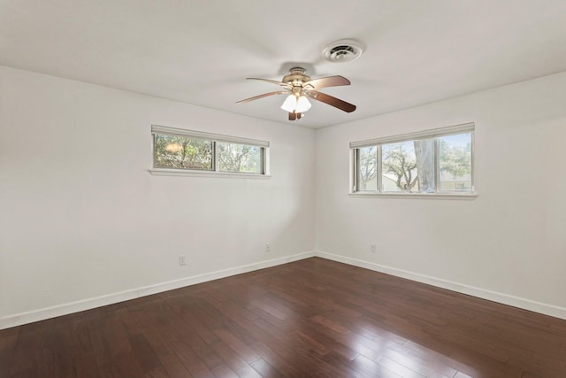 unfurnished room with a wealth of natural light, dark wood-style flooring, visible vents, and baseboards