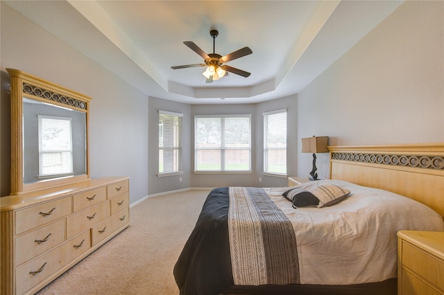 bedroom with a ceiling fan, a tray ceiling, light colored carpet, and baseboards