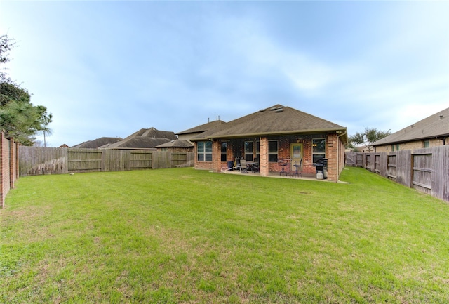 rear view of property featuring a shingled roof, a lawn, a fenced backyard, a patio area, and brick siding