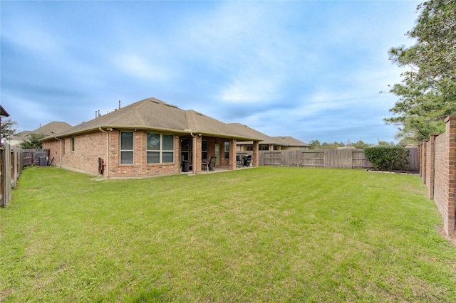 back of property with a patio, a fenced backyard, brick siding, a lawn, and roof with shingles