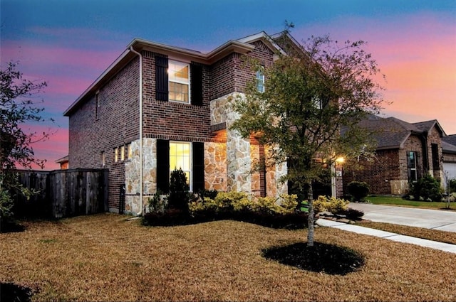 view of front of property with brick siding, fence, stone siding, driveway, and a lawn