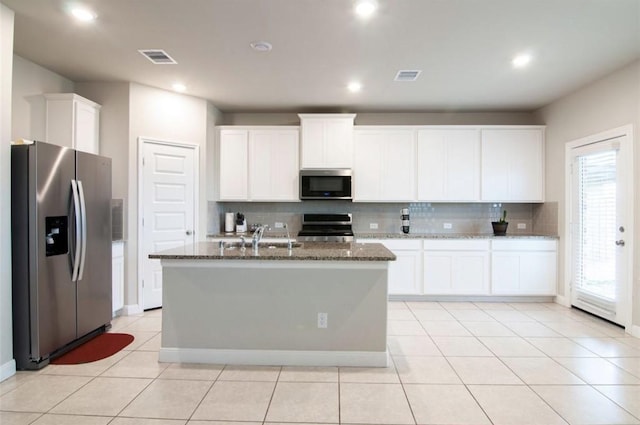 kitchen with a sink, visible vents, appliances with stainless steel finishes, backsplash, and dark stone countertops