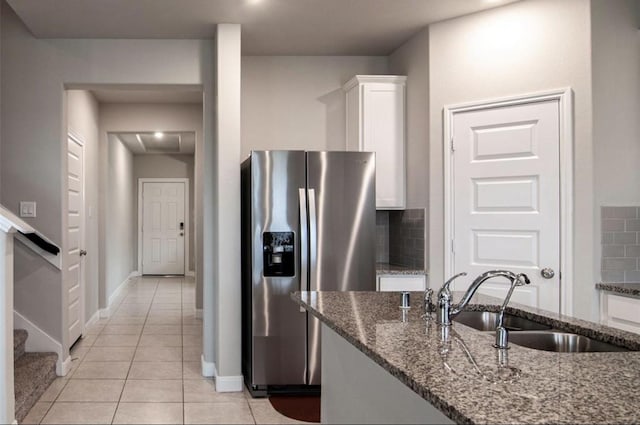 kitchen featuring decorative backsplash, dark stone countertops, white cabinetry, stainless steel refrigerator with ice dispenser, and a sink