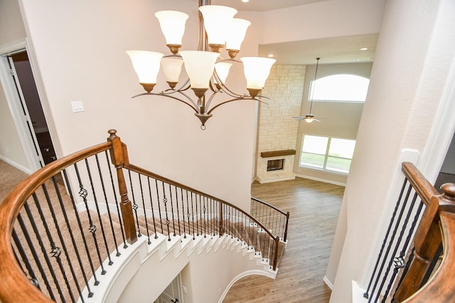 staircase with wood finished floors, baseboards, a high ceiling, a fireplace, and ceiling fan with notable chandelier