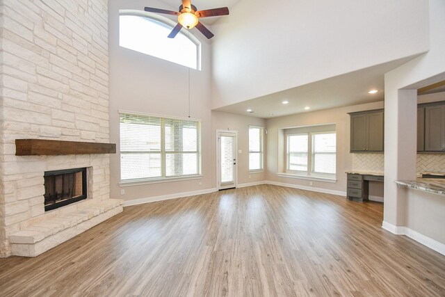 unfurnished living room featuring baseboards, light wood-style floors, a stone fireplace, and ceiling fan