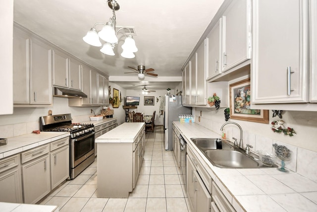 kitchen with tile countertops, stainless steel gas range, a sink, and under cabinet range hood