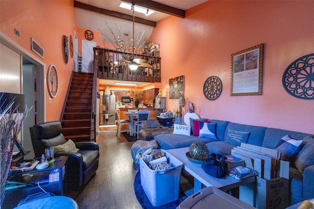 living area featuring wood finished floors, stairs, a high ceiling, beam ceiling, and ceiling fan with notable chandelier