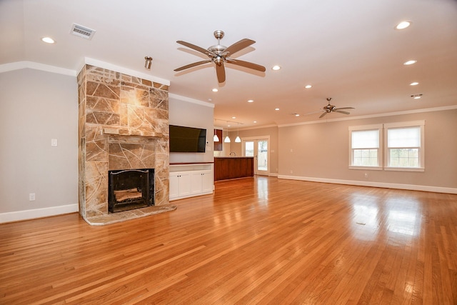 unfurnished living room featuring baseboards, visible vents, light wood-style flooring, a fireplace, and ornamental molding