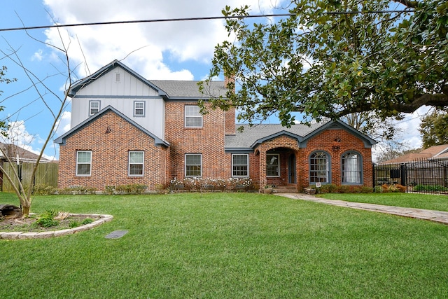 view of front facade with brick siding, a shingled roof, a front lawn, and fence