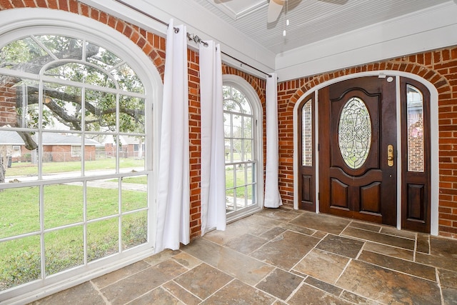 entrance foyer with stone tile flooring, brick wall, and a ceiling fan