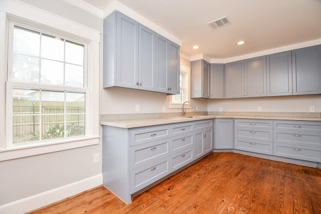 kitchen with wood finished floors, recessed lighting, gray cabinetry, a sink, and light countertops