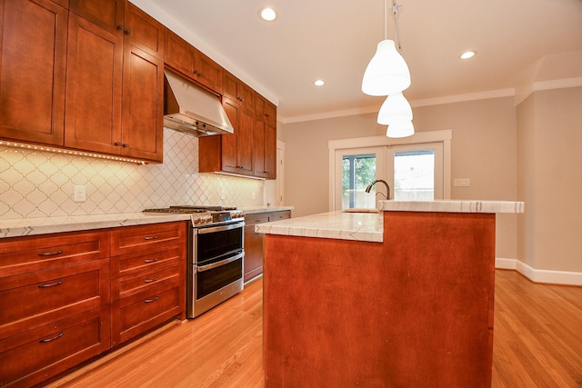 kitchen with double oven range, ornamental molding, light countertops, under cabinet range hood, and backsplash