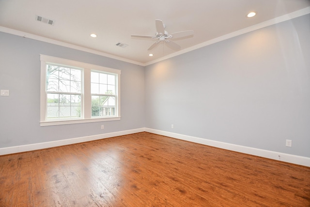 empty room featuring wood finished floors, visible vents, baseboards, and ornamental molding