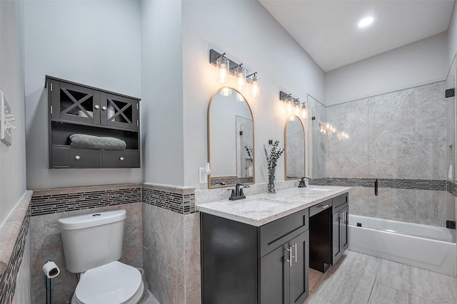 full bath with double vanity, a tub to relax in, toilet, a sink, and tile walls