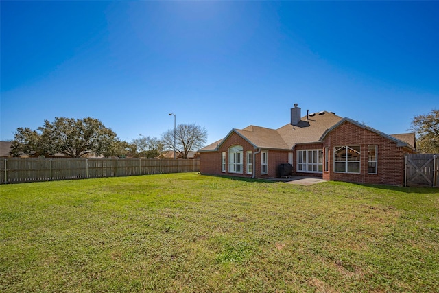 back of property with brick siding, a lawn, a chimney, and a fenced backyard