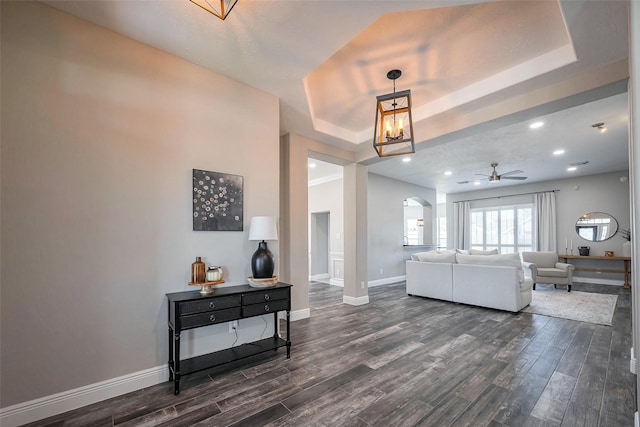 living room featuring a raised ceiling, dark wood finished floors, and baseboards