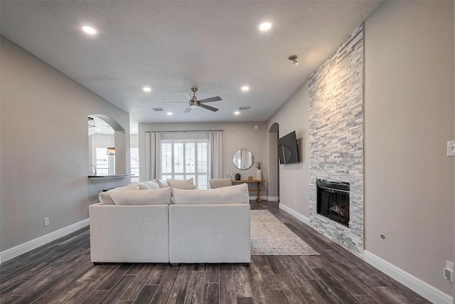 living area featuring baseboards, a fireplace, arched walkways, and dark wood-type flooring