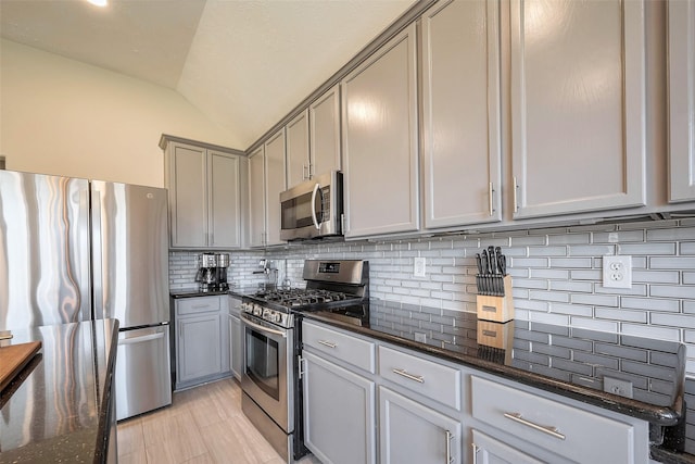 kitchen with appliances with stainless steel finishes, vaulted ceiling, dark stone countertops, and tasteful backsplash