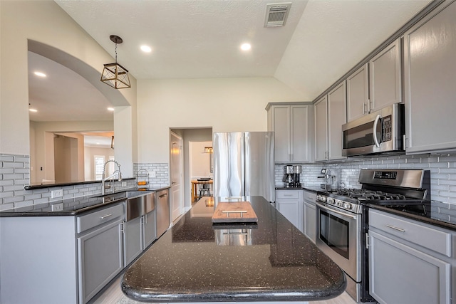 kitchen with arched walkways, gray cabinetry, a kitchen island, visible vents, and appliances with stainless steel finishes