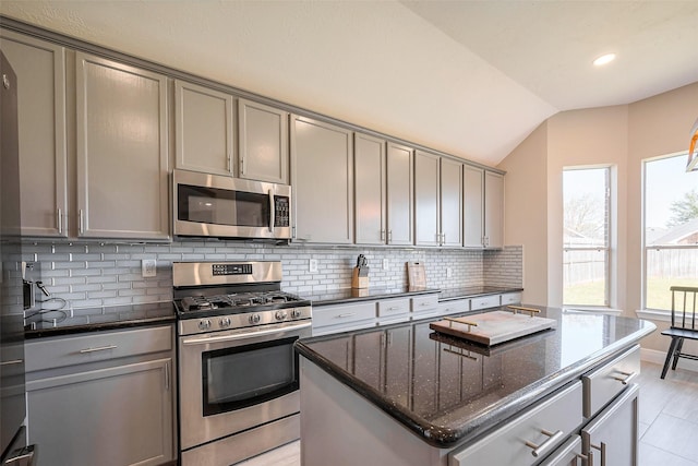 kitchen with lofted ceiling, appliances with stainless steel finishes, gray cabinets, decorative backsplash, and dark stone counters