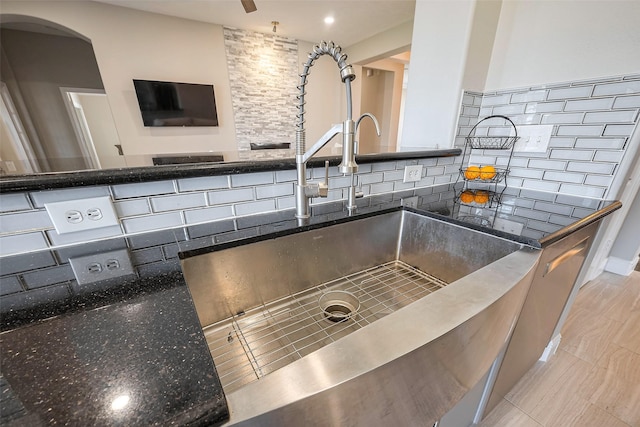 details with decorative backsplash, arched walkways, a sink, and dark stone countertops