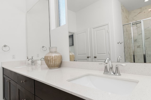 full bath with a sink, a marble finish shower, and double vanity