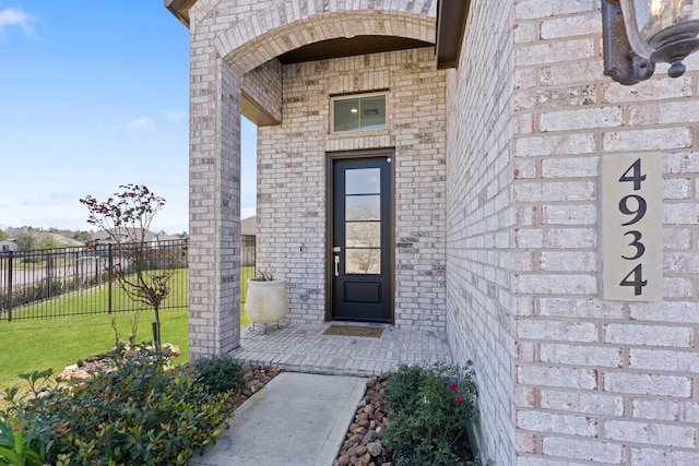 entrance to property featuring brick siding, a yard, and fence