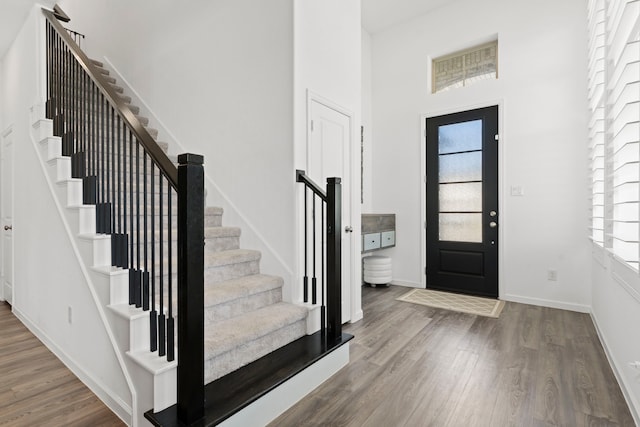 foyer with stairway, baseboards, wood finished floors, and a towering ceiling