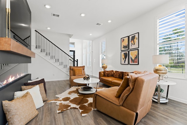 living area featuring visible vents, stairway, recessed lighting, wood finished floors, and a glass covered fireplace