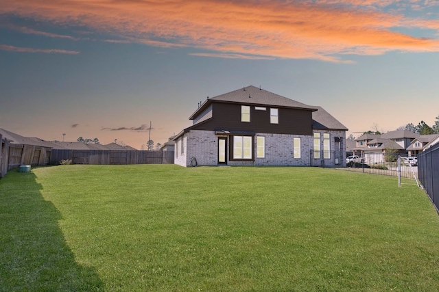 rear view of house with brick siding, a lawn, and a fenced backyard