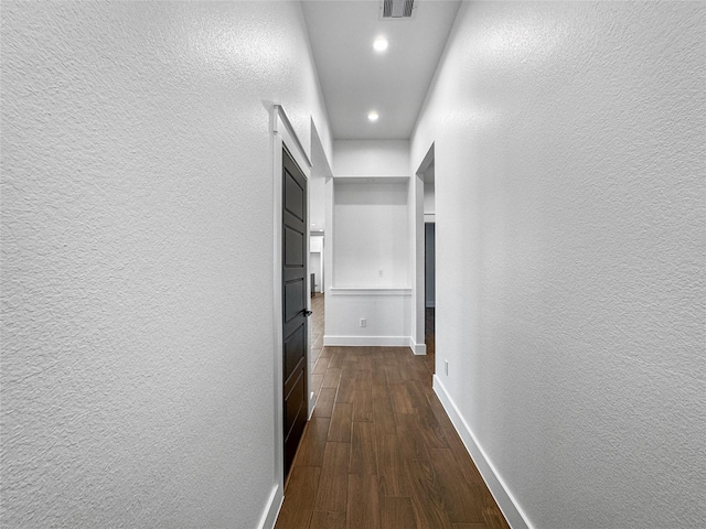 hall with dark wood-style floors, recessed lighting, visible vents, a textured wall, and baseboards