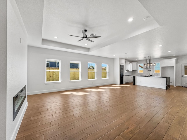 unfurnished living room featuring baseboards, a tray ceiling, wood finished floors, and a glass covered fireplace