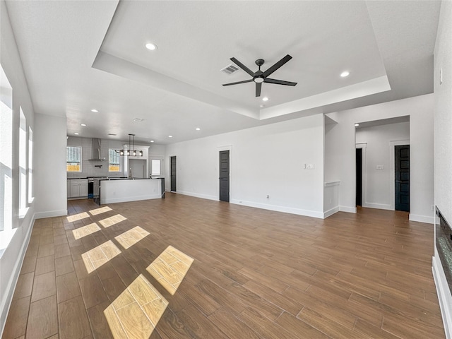 unfurnished living room with a tray ceiling, visible vents, recessed lighting, and wood finished floors