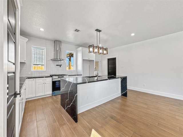 kitchen with visible vents, wall chimney range hood, stainless steel gas range, backsplash, and dark countertops