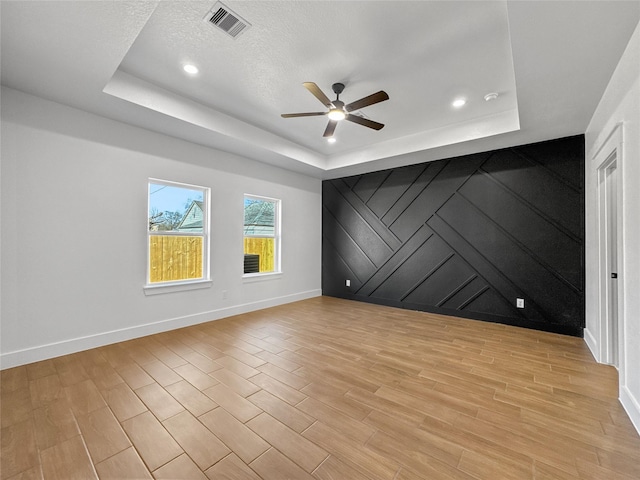 empty room featuring light wood-type flooring, baseboards, visible vents, and a raised ceiling