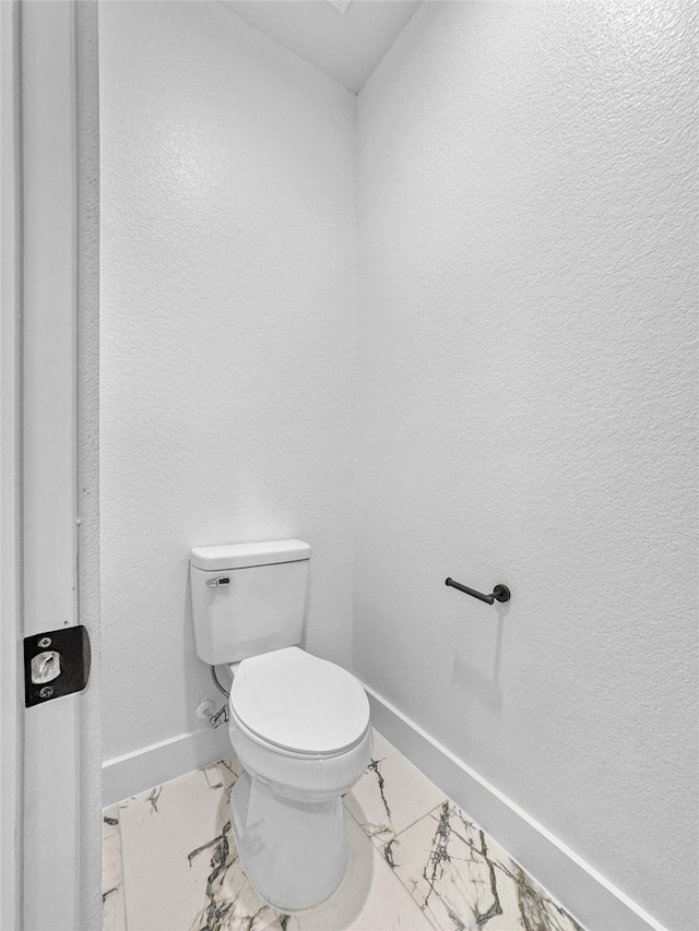 bathroom with toilet, marble finish floor, and baseboards