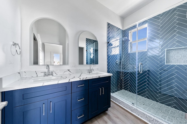 bathroom featuring double vanity, wood finished floors, a sink, and a shower stall