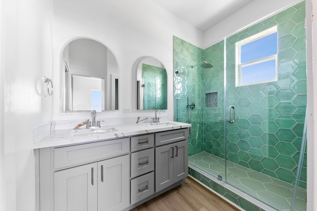 bathroom featuring double vanity, wood finished floors, a stall shower, and a sink