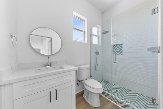 bathroom featuring toilet, wood finished floors, vanity, baseboards, and a stall shower