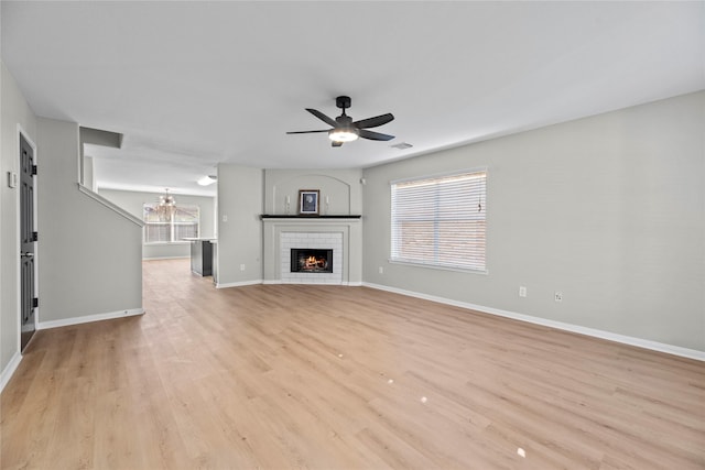 unfurnished living room with ceiling fan with notable chandelier, a fireplace, a wealth of natural light, and light wood-style floors