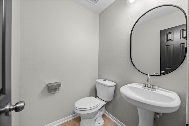 half bath with a sink, wood finished floors, toilet, and baseboards