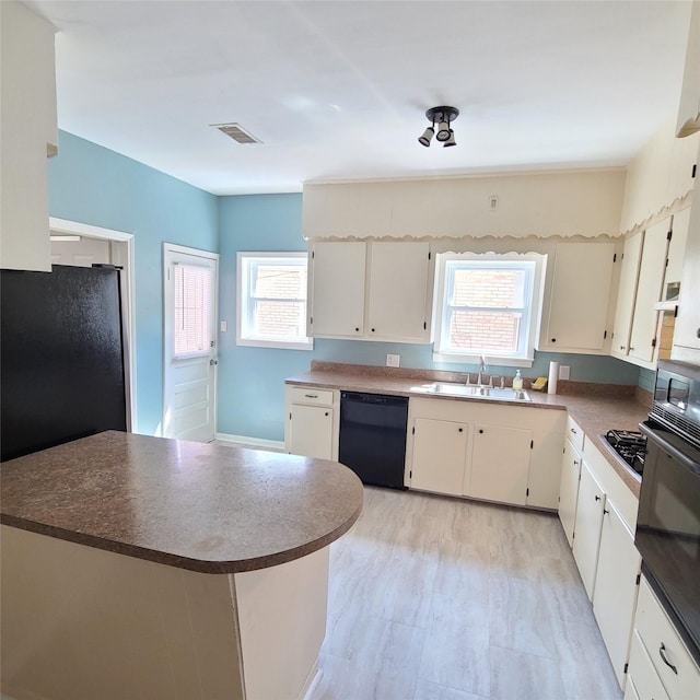 kitchen with visible vents, dark countertops, black appliances, white cabinetry, and a sink