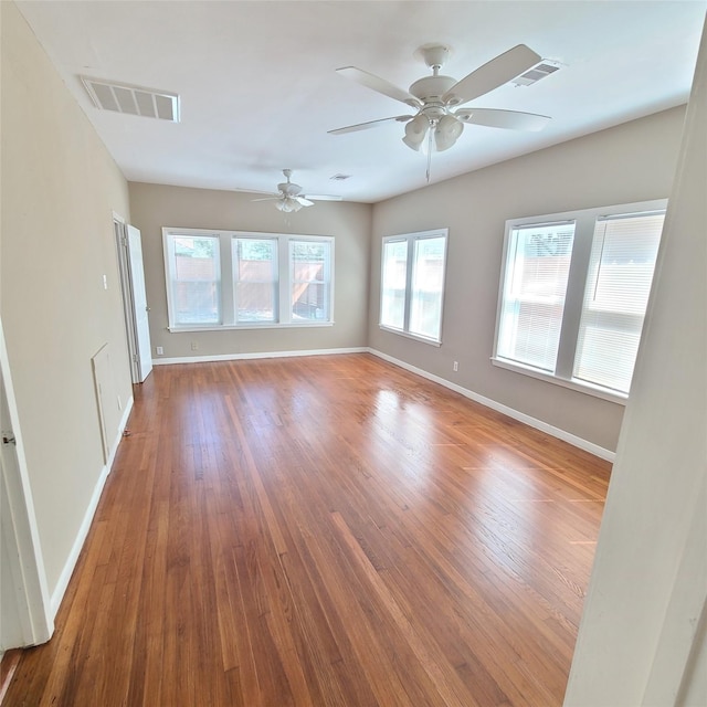 empty room with wood finished floors, visible vents, and baseboards