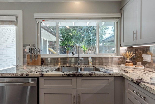 kitchen featuring dishwasher, tasteful backsplash, a sink, and light stone countertops